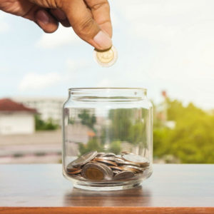 A person is putting money in a glass jar.